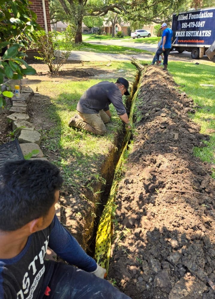 Three Allied Foundation workers installing yellow BioBarrier root barrier fabric in a trench beside a lawn